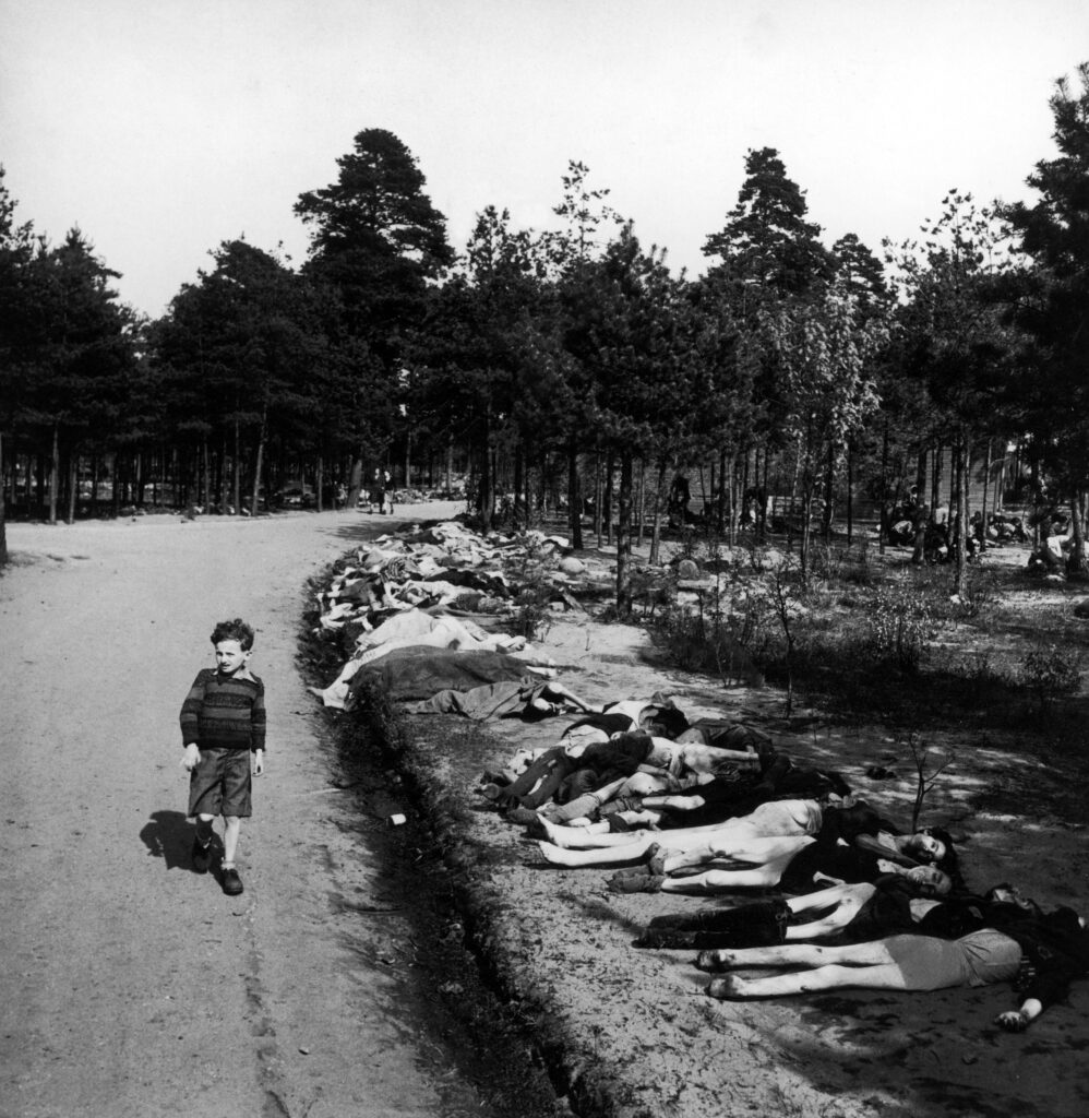 Young boy dressed in shorts walks along a dirt road lined with the corpses of hundreds of prisoners who died at the Bergen-Belsen extermination camp, near the towns of Bergen and Celle, Germany, April 20, 1945. Please note that this image was edited to obscure nudity. (Photo by George Rodger/The LIFE Picture Collection via Getty Images)