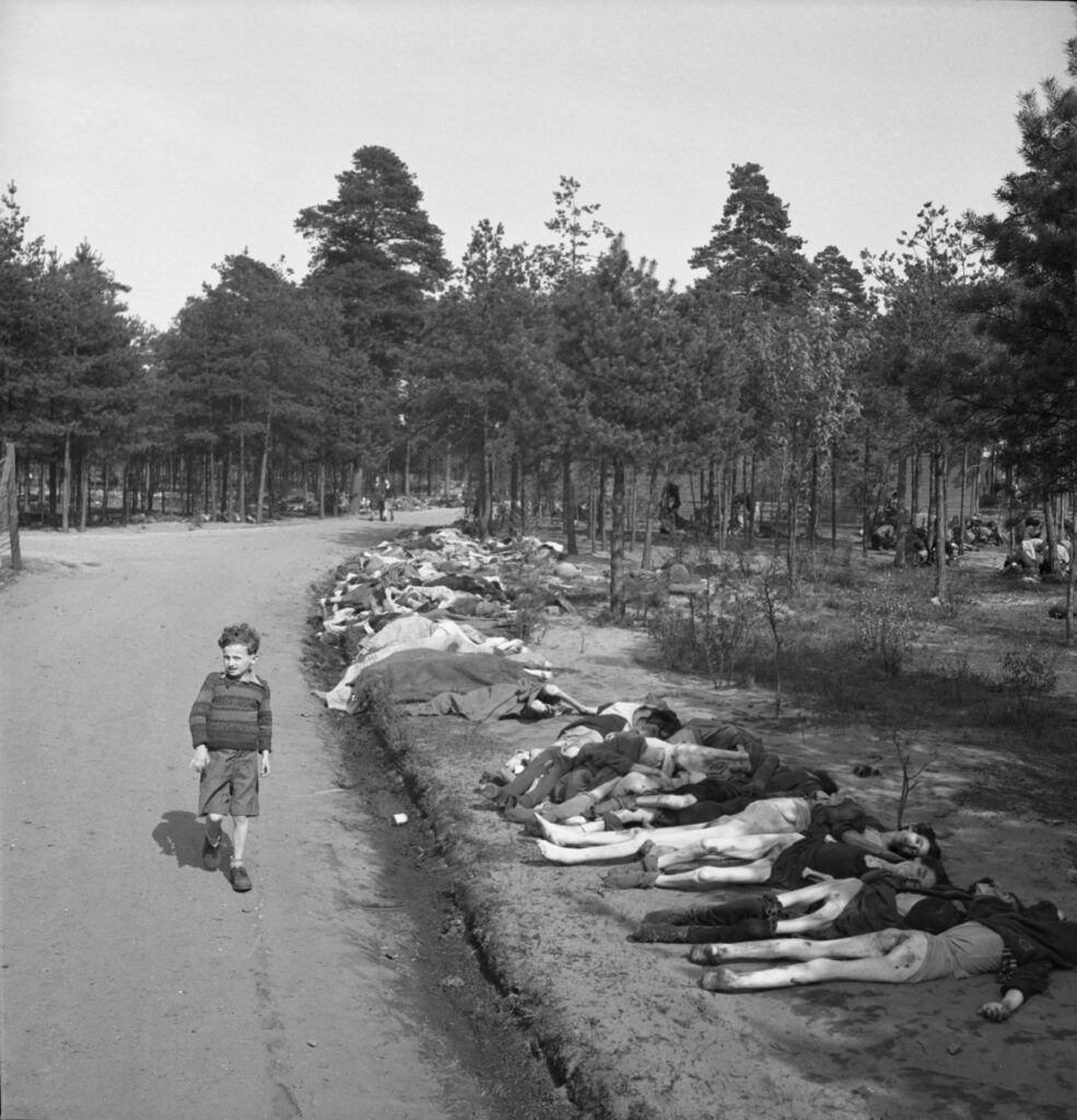 Young boy dressed in shorts walks along a dirt road lined with the corpses of hundreds of prisoners who died at the Bergen-Belsen extermination camp, near the towns of Bergen and Celle, Germany, April 20, 1945. (Photo by George Rodger/The LIFE Picture Collection via Getty Images).